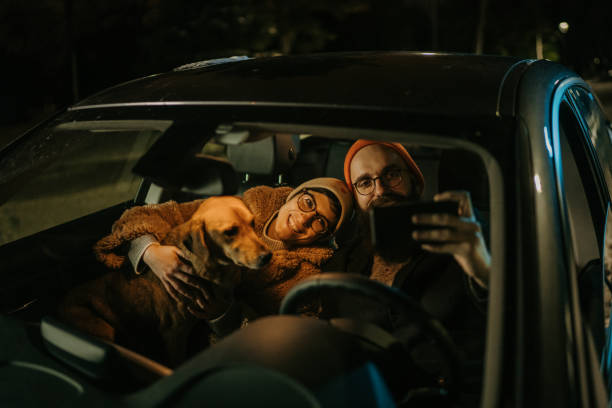 istock Young smiling couple sitting at car with their dog while they making selfie 1365029552