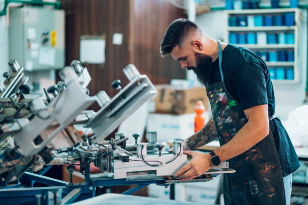 männlicher arbeiter mit einer druckmaschine in einer werkstatt - serigraphy stock-fotos und bilder