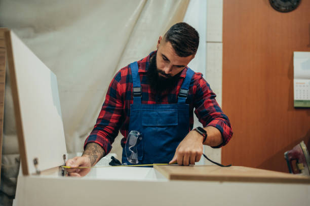 istock Young male carpenter working in workshop and measuring with meter 1365037593