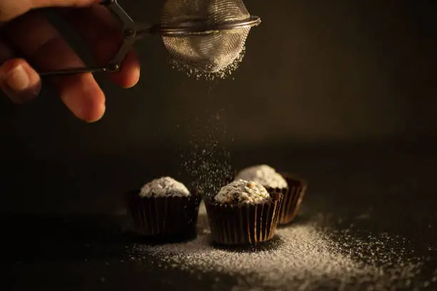 Female hands sprinkle home made chocolate sweets with powdered sugar on dark background