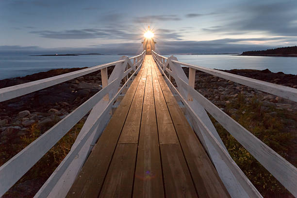 Marshall Point Lighthouse at sunset, Maine, USA Frontal view over wooden bridge with wide perspective on Marshall Point Lighthouse near small village Port Clyde in Maine, USA. Cloudy and dark sky. Marshall Point Lighthouse was first lit in 1857 and became famouse when appeared in the 1994 film Forrest Gump. light at the end of the tunnel stock pictures, royalty-free photos & images