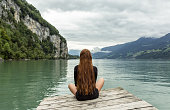 istock Relaxed woman sitting alone on a dock facing the beautiful lake view. 1365045265