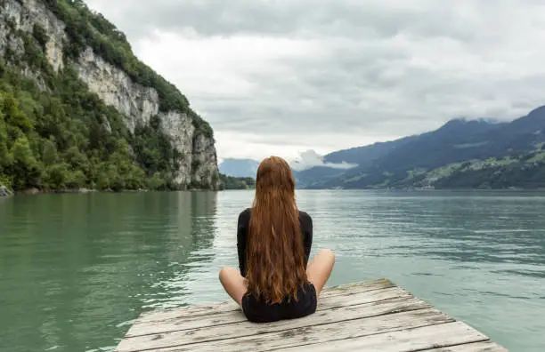 Photo of Relaxed woman sitting alone on a dock facing the beautiful lake view.