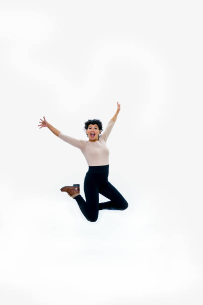 a beautiful middle aged hispanic woman jumping in the air against a white background while wearing a tan top, black pants, and leather boots. - native american north american tribal culture women mature adult imagens e fotografias de stock