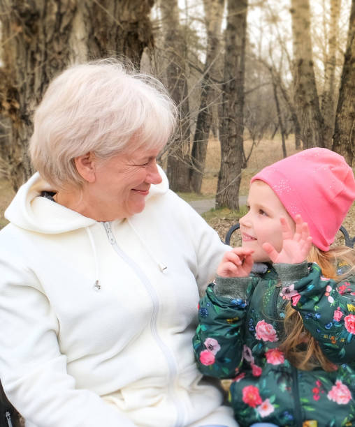 nonna con la sua nipotina che abbraccia e parla seduta su una panchina nel parco - senior adult winter senior women daughter foto e immagini stock