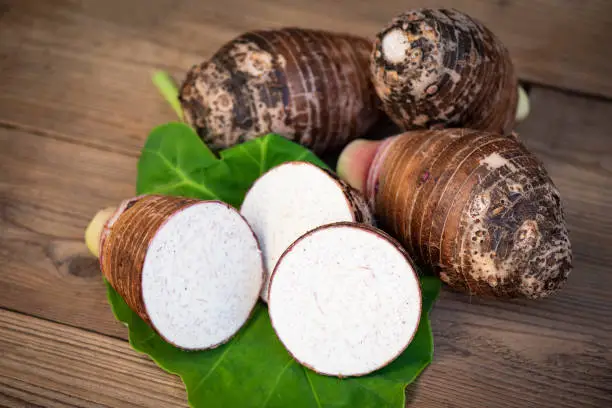 Fresh raw organic taro root ready to cook, Taro root with half slice on taro leaf and wooden background