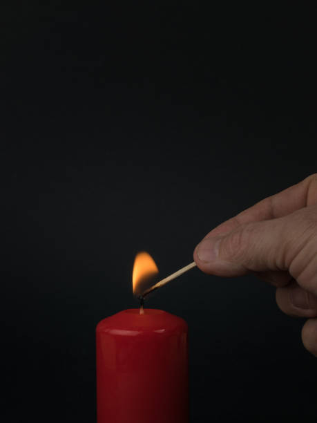istock A man lights a red wax candle with a match on a black background. 1365053869