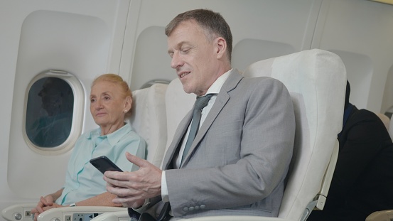 Senior passenger man using smartphone on airplane while traveling for safe flight, Businessman sitting inside plane watching video on mobile phone during his business trip