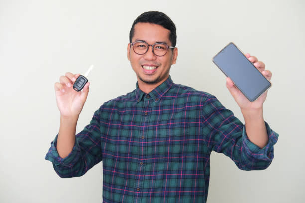 빈 휴대 전화 화면을 보여주고 자동차 키를 들고있는 동안 행복한 미소 성인 아시아 남자 - baru 뉴스 사진 이미지