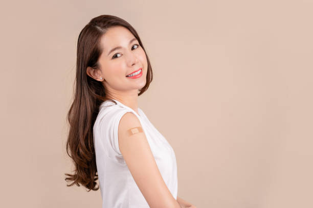istock Coronavirus vaccination advertisement. Happy Young beautiful asian woman getting vaccinated showing arm with plaster bandage after Covid-19 vaccine injection posing on background, Smiling to camera. 1365062015
