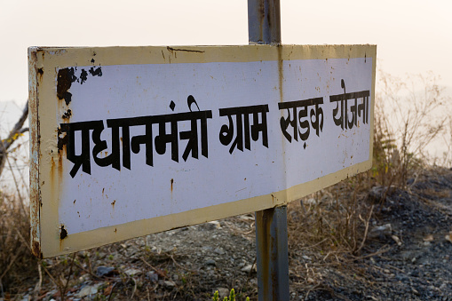 A road side bill board addressing a rural plan for road construction in India written in hindi which translates \