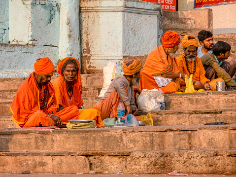 Varanasi, India - November 13, 2015. Hindu men wearing traditional saffron-colored sadhu clothing and headwear sit on ghats near the Ganges River with with donation bowls.