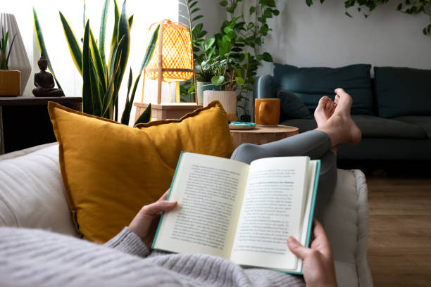 pov di giovane donna che si rilassa a casa leggendo un libro sdraiata sul divano - volume foto e immagini stock