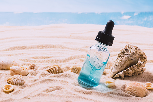 Glass bottle with serum gel cosmetic product with air bubbles on the background of seashells and sea beach sand. Abstract podium from natural materials product presentation on a sandy background