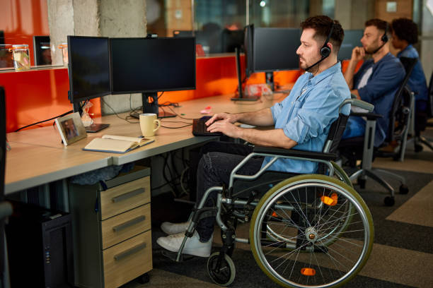 istock Handicapped computer programmer in wheelchair at his office desk 1365072483