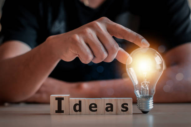 istock hand touching on light bulb on wood block with Word Ideas, 1365073608
