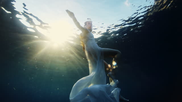 SLO MO Young woman in white dress swims in the sea at sunset