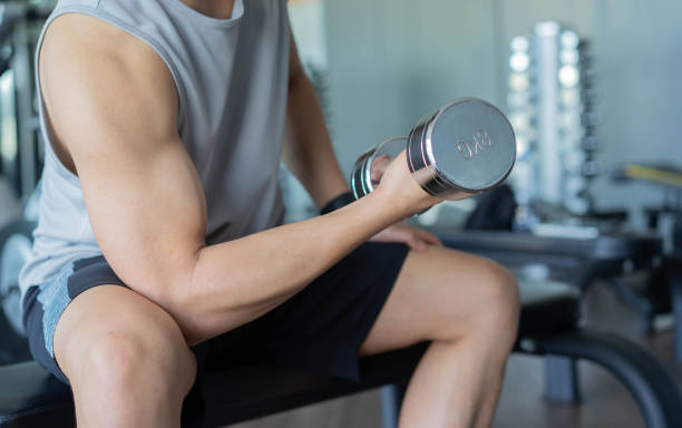 escena de cerca joven asiático sosteniendo mancuerna en mano para jugar prensa de bíceps para ganar músculo en el gimnasio por la tarde, concepto de estilo de vida saludable - body care asian ethnicity body building toughness fotografías e imágenes de stock