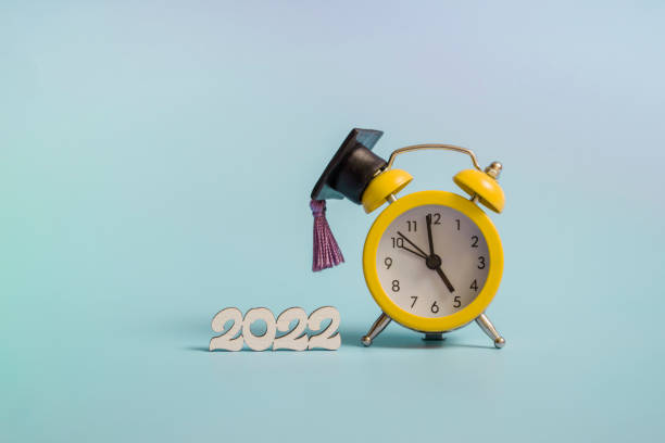 istock Yellow alarm clock with graduation cap on blue background closeup with copy space 1365076075