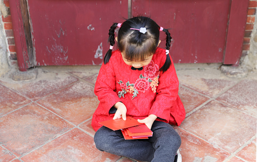 two asian twins girls wearing cheongsam make a New Year’s visit. They holding New Year’s Money and Spring couplets. Traditional custom of chinese new year.