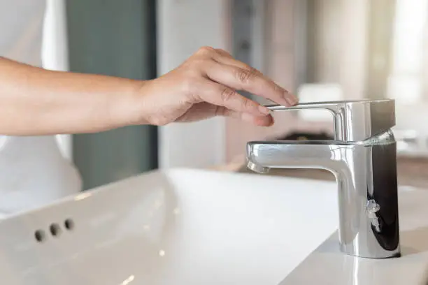 Photo of Close up Woman open chrome faucet washbasin to washing hands rubbing with soap for corona virus at water tap. Faucet and water drop off. Bathroom interior with sink basin and water tap. Tap water down.