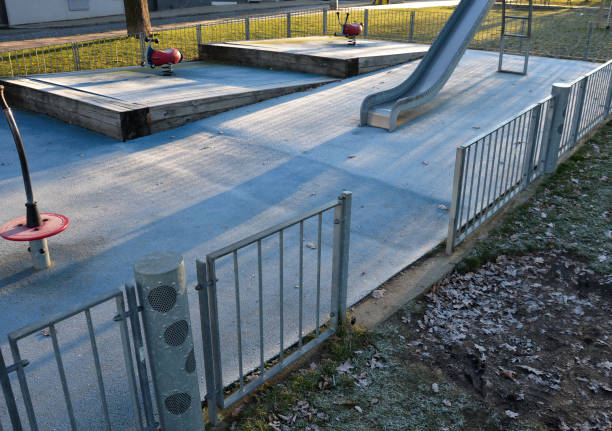 istock playground with stainless steel slide and blue rubber surface. stepped terraces bordered by massive beams. Galvanized fencing with a gate against dogs. swings on a steel spring backyard nursery in the park 1365083267