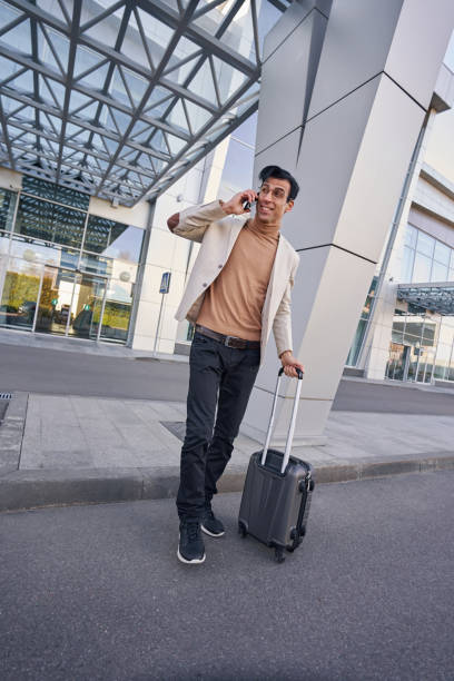 istock Man crossing road with luggage while talking on phone 1365084253