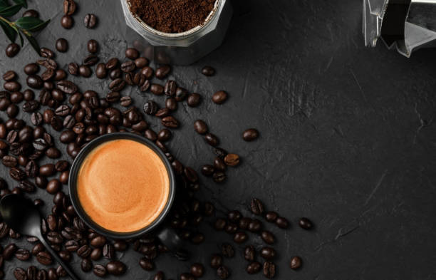 Aromatic espresso coffee in a cup on a black table next to a coffee pot. Coffee beans and coffee ingredients on the table. Top view, place for text. Italian style breakfast idea. stock photo
