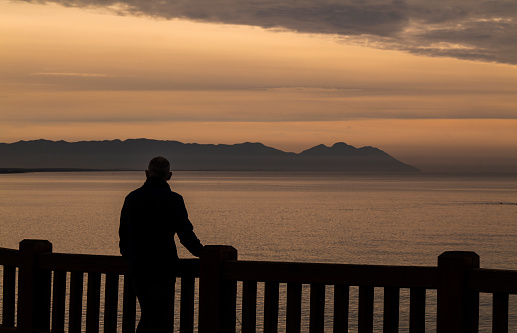 Silhouette of man standing on railing looking at sea view during sunrise. Almeria, Spain