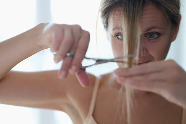 A woman scissors cuts her own hair, close-up A woman cuts herself a lock of hair, close-up. Doing your own bangs at home during a pandemic. Haircut at home bangs hair stock pictures, royalty-free photos & images
