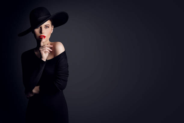 modelka fashion woman w kapeluszu pokazująca shh znak cichego gestu wkładając palec w czerwone usta. elegancka dama w czarnej sukience na szarym tle studio - finger on lips whispering secrecy silence zdjęcia i obrazy z banku zdjęć