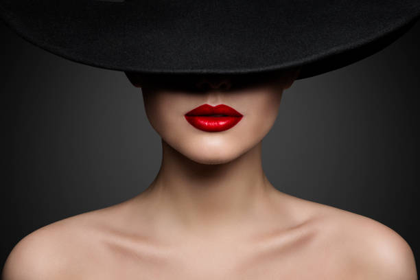 rote lippen make up nahaufnahme. mysteriöses modefrauengesicht, das von einem hut mit schwarzer krempe verdeckt wird. elegantes retro lady fine art porträt über grauem hintergrund - roter lippenstift stock-fotos und bilder