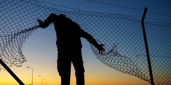Refugee man running behind fence
