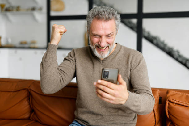Senior grey-haired man is using smartphone for watching sports soccer match