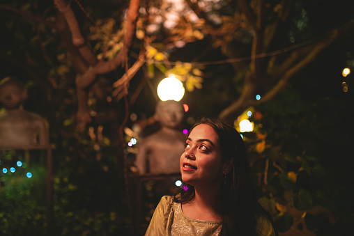 A smiling girl walks around the streets at night appreciating the Diwali festival decorative lights in the city. Festive ambience at Indian wedding party.