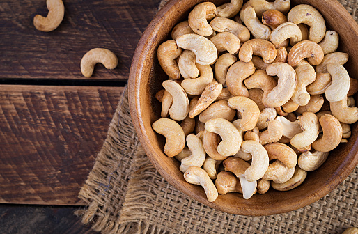 Tasty cashew nuts in bowl on wooden table. Top view, overhead