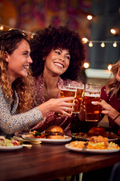 gruppo multiculturale di amiche che si godono la serata fuori a mangiare e bere nel ristorante - friendship drinking beer group of people foto e immagini stock