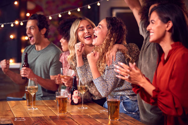 gruppo di amici che festeggiano guardando il gioco sportivo o la partita bevendo insieme al bar - bar foto e immagini stock