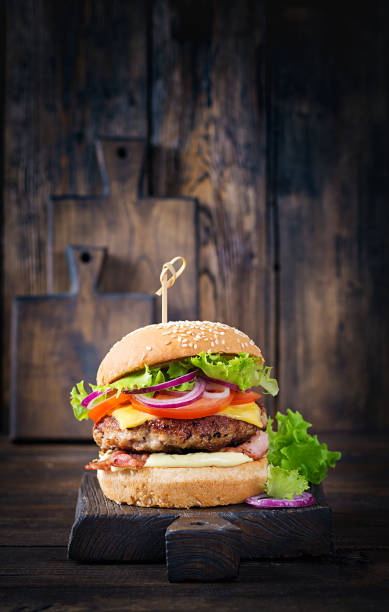 Hamburger with bacon, turkey burger meat, cheese, tomato and lettuce on wooden background. Tasty burger. Close up stock photo