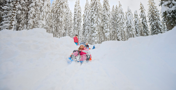 Girls enjoying tobogganing on snowy hill during winter.