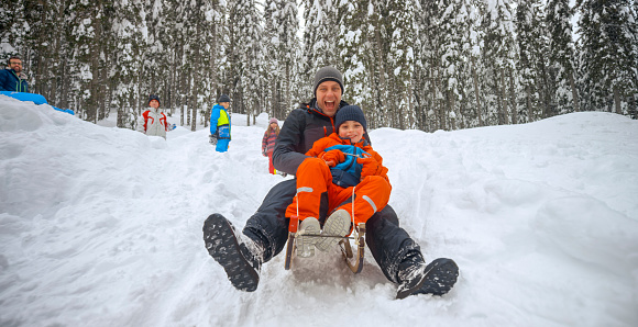 Father and son enjoying tobogganing on snowy hill during winter.