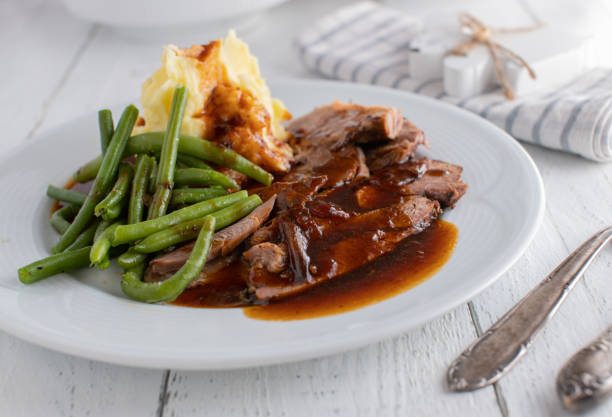 Plate with roast meat, gravy, green beans and mashed potatoes Homemade dish for easter holiday with sliced turkey shanks, delicious gravy, vegetable and potato puree. Served on a white plate on wooden table celebrity roast stock pictures, royalty-free photos & images