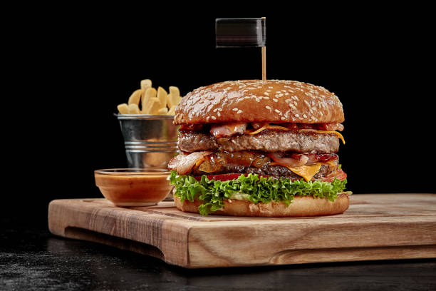 Burger with two patties, bacon, cheese, caramelized onions, tomatoes and greens served with fries and aioli sauce stock photo