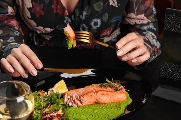 istock Female hands holding knife and fork with baked trout steak piece served with mashed peas, salad, lemon 1365105641