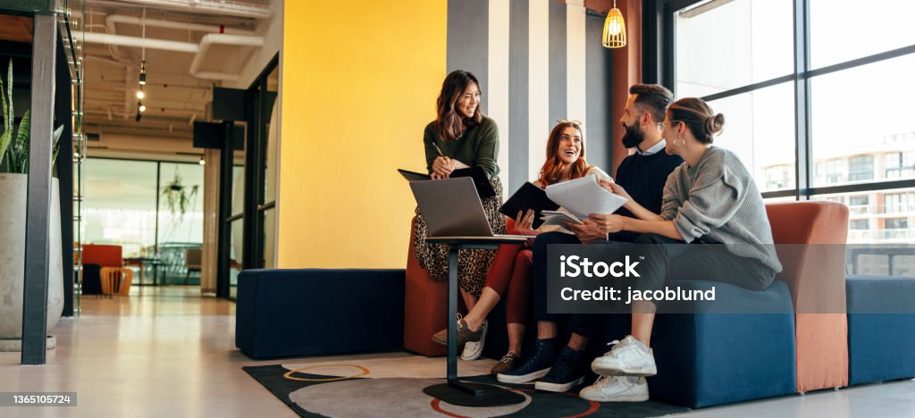 Multicultural businesspeople working in an office lobby Multicultural businesspeople working in an office lobby. Group of happy businesspeople smiling while sitting together in a co-working space. Young entrepreneurs collaborating on a new project. Office Stock Photo