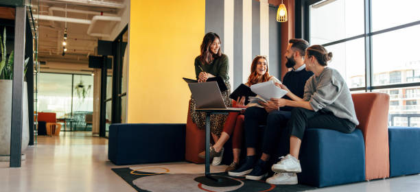 Multicultural businesspeople working in an office lobby Multicultural businesspeople working in an office lobby. Group of happy businesspeople smiling while sitting together in a co-working space. Young entrepreneurs collaborating on a new project. office stock pictures, royalty-free photos & images