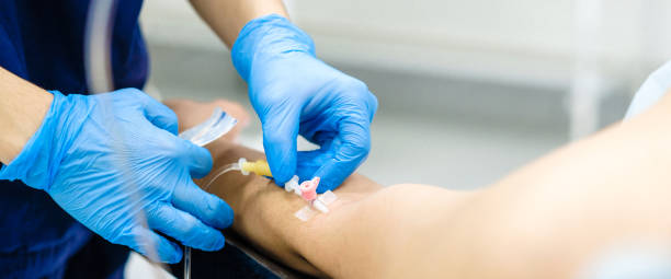 Inserting the dropper needle into the patient's arm. Inserting the dropper needle into the patient's arm. Selective focus. Doctor's hands in sterile gloves install a catheter for intravenous administration of drugs to a patient. Widescreen image. catheter photos stock pictures, royalty-free photos & images