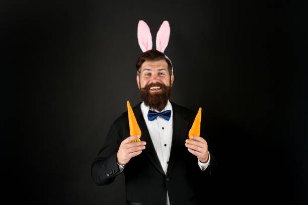 istock Rabbit bringing Easter carrots. Easter rabbit black background. Bearded man hold carrots. Happy businessman wear rabbit ears. Rabbit costume party. Bunny or hare. Easter symbol. Holiday celebration 1365106976