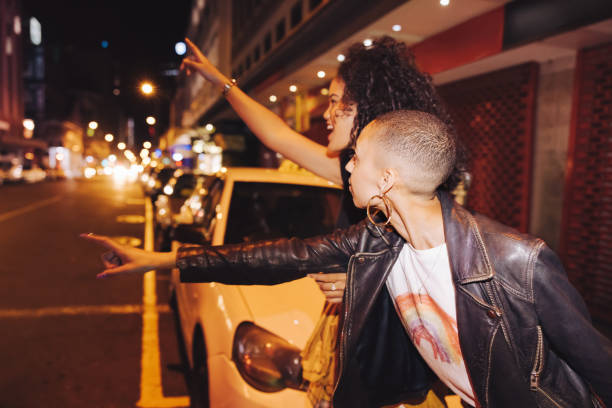 two friends hailing a taxi in the city - chamada de fotografia imagens e fotografias de stock