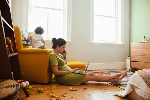 Mom working from home during quarantine. Working mom speaking on the phone while sitting in her son's play area. Single mother communicating with her business clients during lockdown.